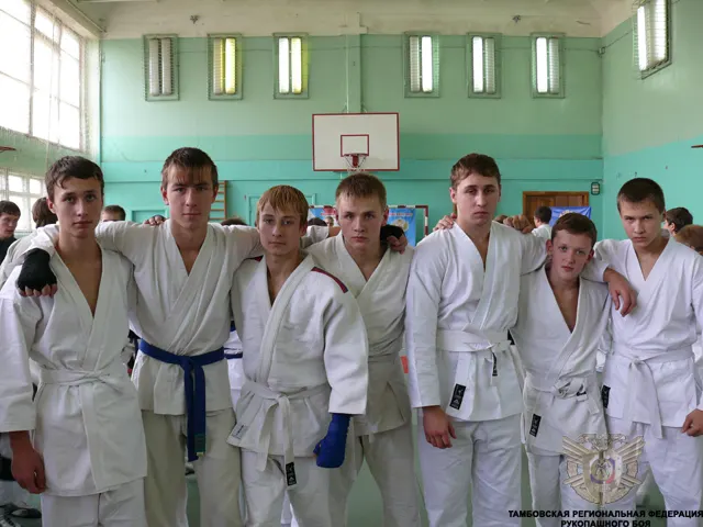 Группа спортсменов в белых кимоно стоит в ряд, обнявшись, в спортивном зале с зелеными стенами и баскетбольным щитом