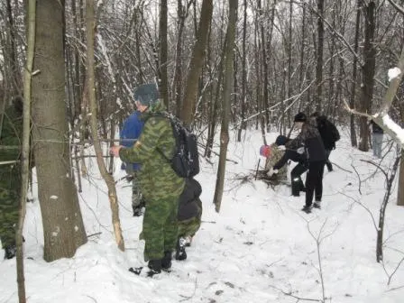 Люди в камуфляже и зимней одежде в заснеженном лесу, один с рюкзаком