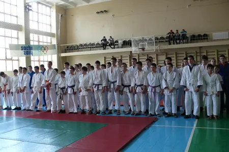 Шеренга юных спортсменов в белых кимоно с поясами разных цветов в спортзале