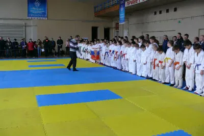 Юные спортсмены в белых кимоно стоят в строю на татами в спортивном зале