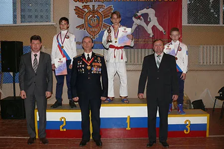 Награждение юных спортсменов на пьедестале, перед ними стоят трое мужчин